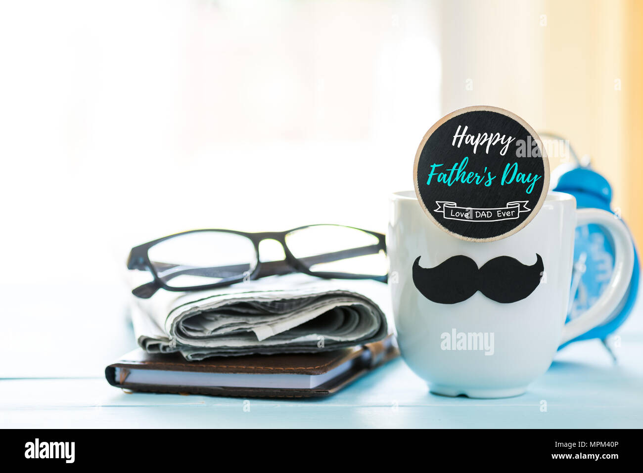 Happy fathers day concept. coffee cup with black paper mustache, heart tag and newspaper, glasses on wooden table background. Stock Photo