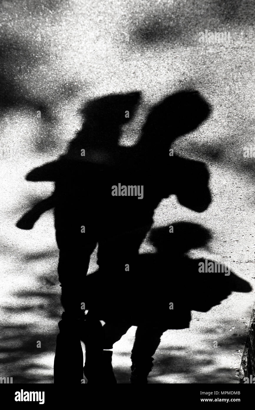 Blurry shadow silhouette of a family , father carrying  a toddler child on hips ,  daughter walking behind them , in black and white Stock Photo