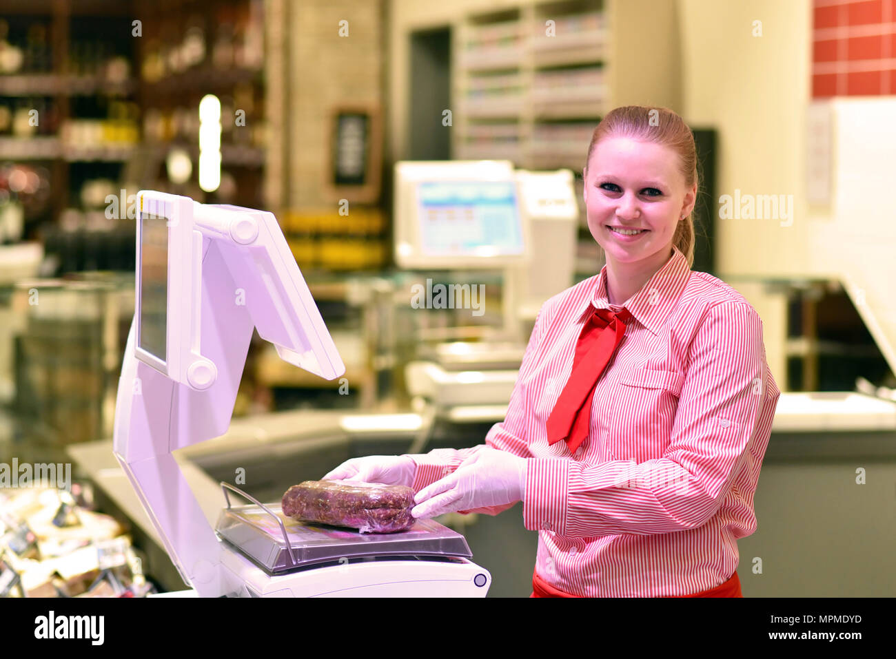 young saleswoman at the fresh counter in the supermarket - sale of cheese and meat Stock Photo
