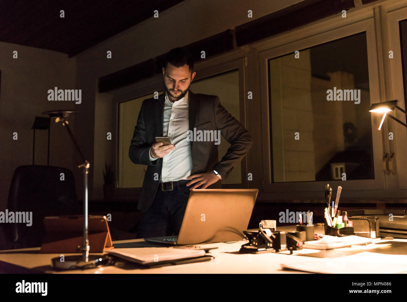 Businessman standing in office at night using smartphone Stock Photo