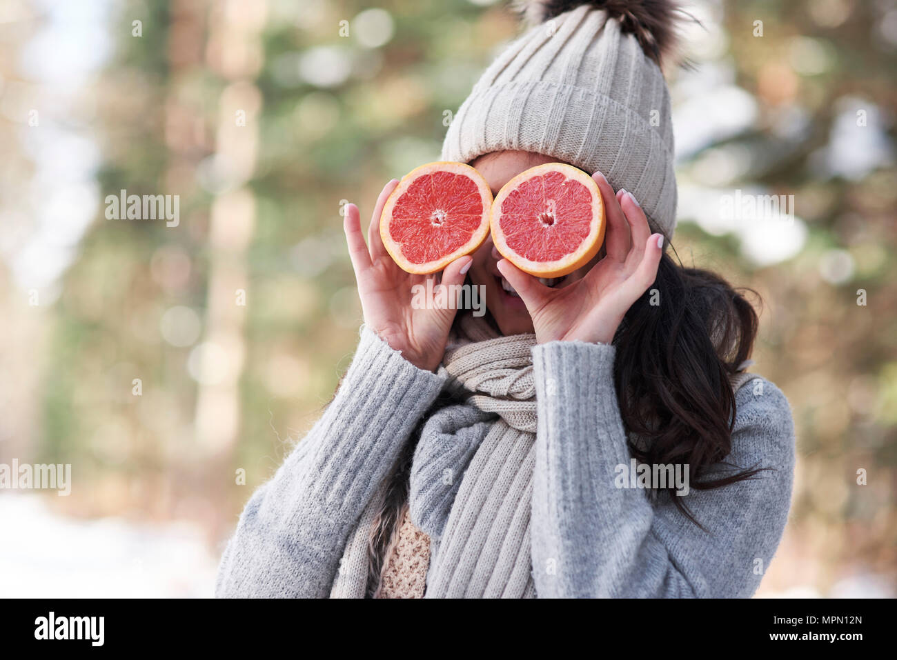 Laughing young woman wearing knitwear covering her eyes with halves of grapefruit Stock Photo