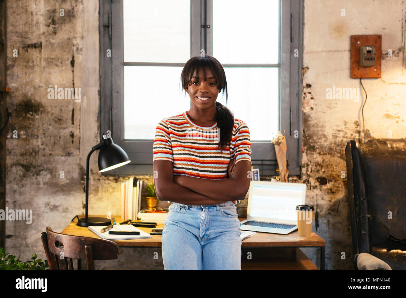 Portrait of smiling young woman standing front of desk in a loft Stock ...