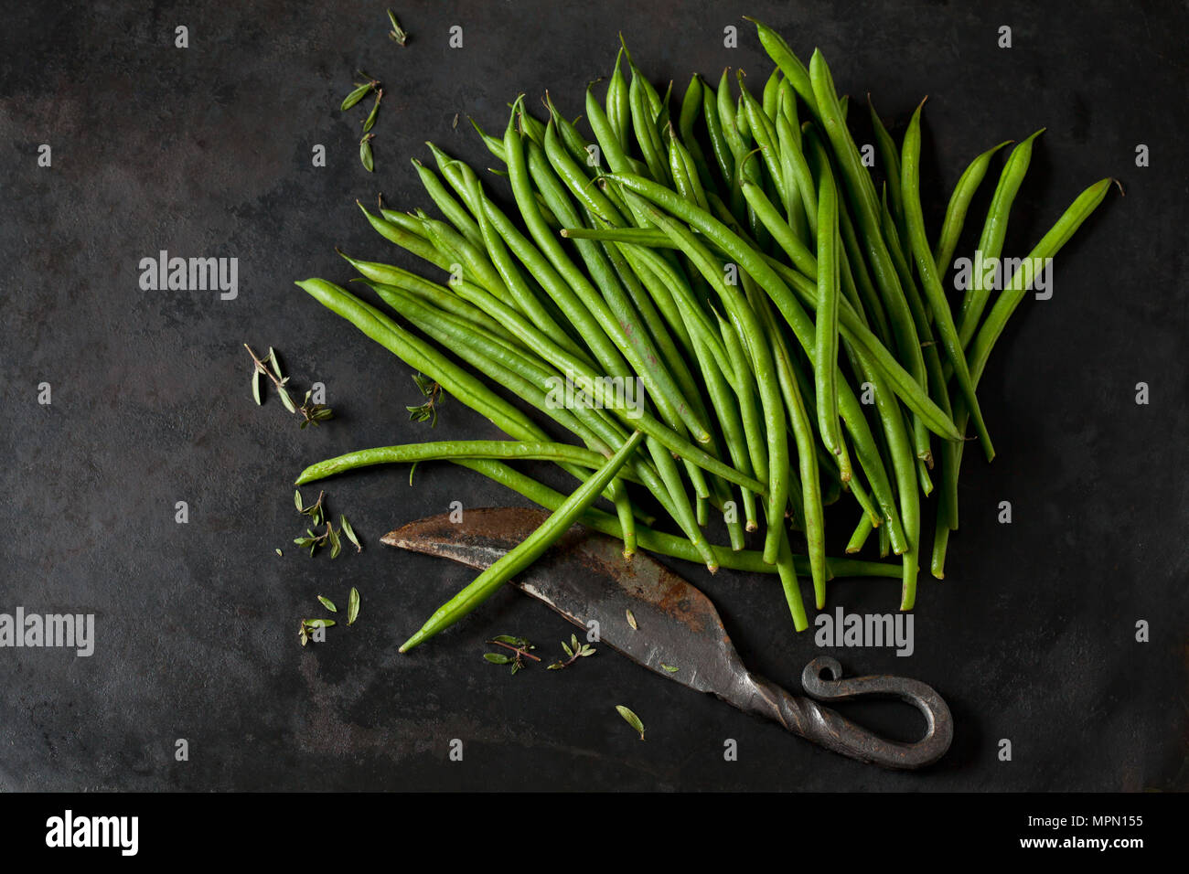 Needle beans, sayory and an old knife on dark metal Stock Photo