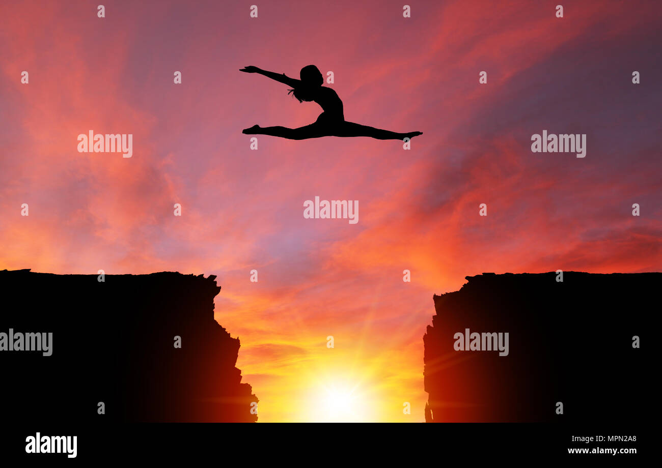 Silhouette of girl dancer in a split leap over dangerous cliffs with dramatic sunset or sunrise background and copy space. Concept of faith, conquerin Stock Photo