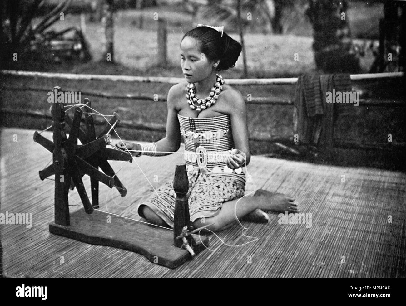 A Dayak girl at her spinning wheel, 1902. Artist: Unknown. Stock Photo