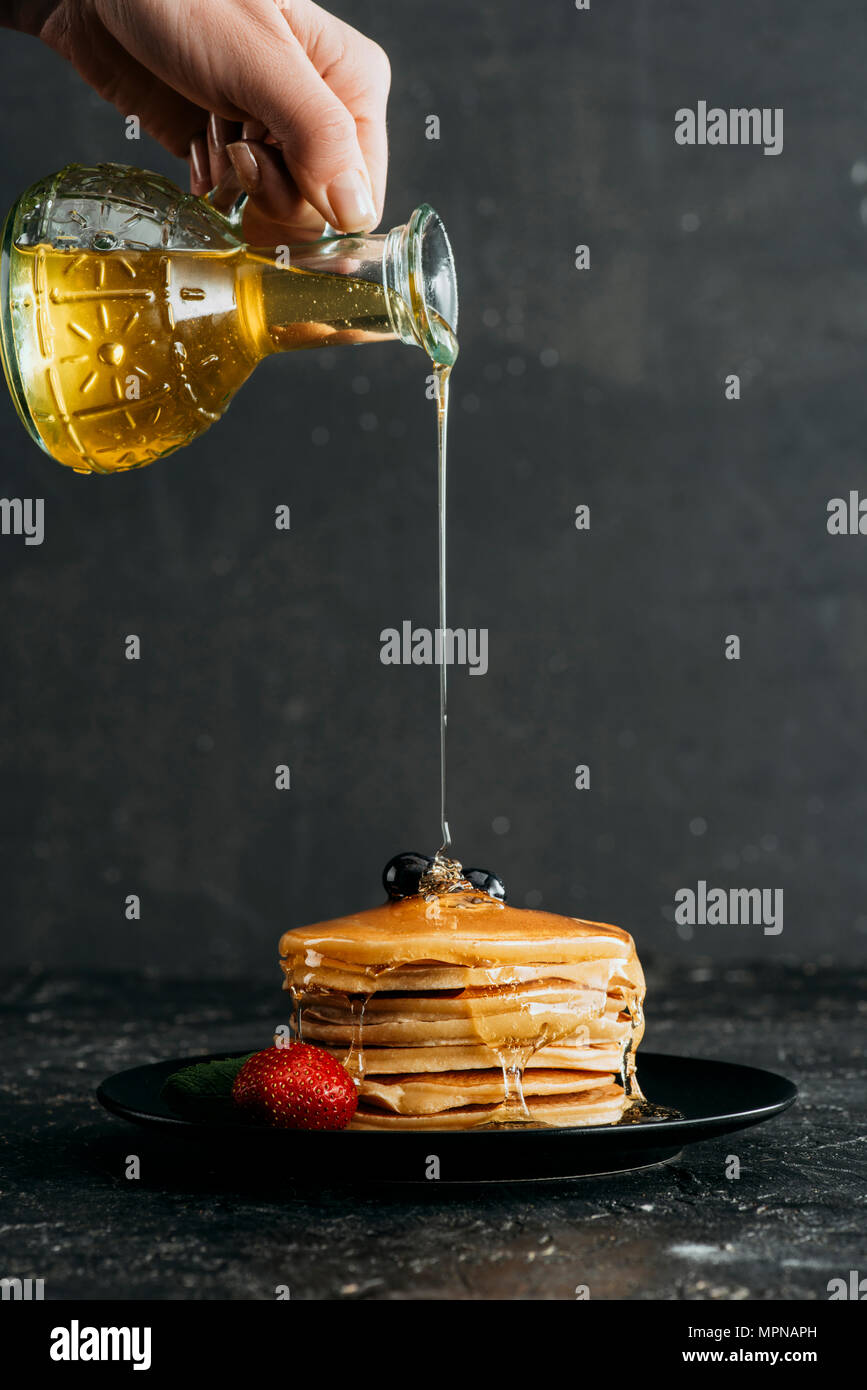 cropped shot of woman pouring maple syrup onto stack of freshly baked pancakes Stock Photo
