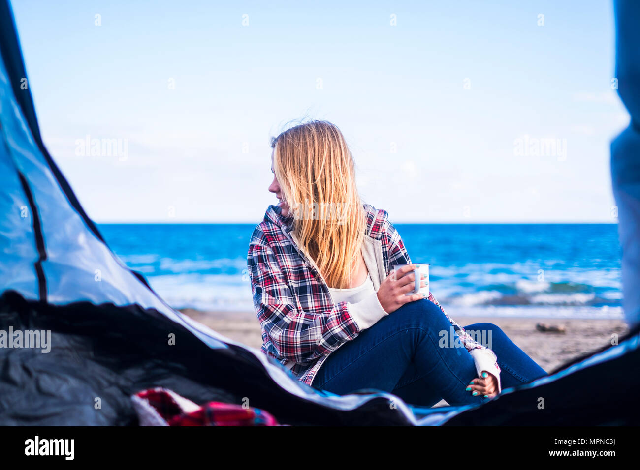 alternative life and vacation concept for blonde cute girl sit down looking at the ocean on the door of her tent. Tenerife locetion. Stock Photo
