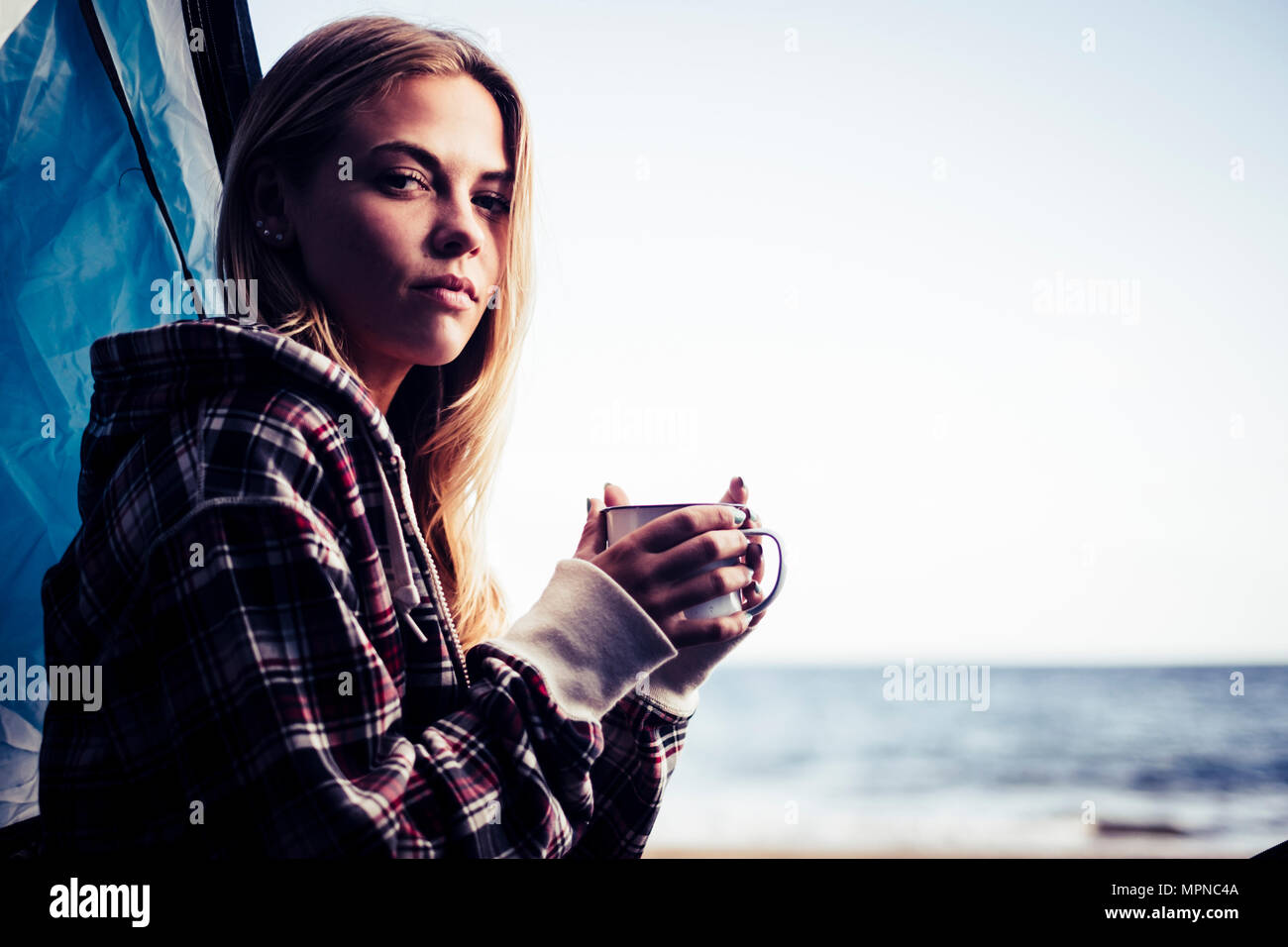 alternative life and vacation concept for blonde cute girl sit down looking at the ocean on the door of her tent. Tenerife locetion. Stock Photo