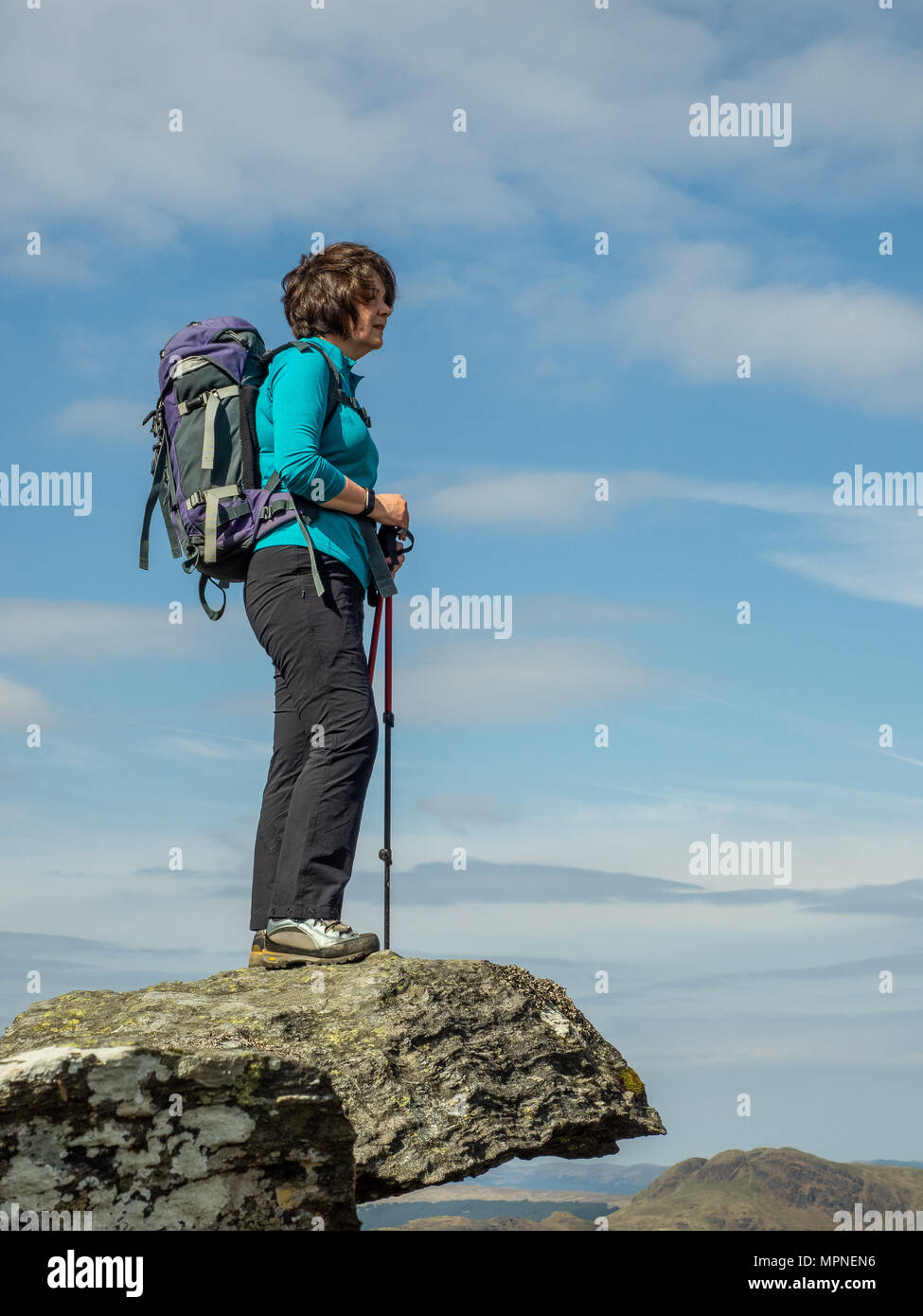 An active senior lady standing on rocks at the top of a mountain in the Scottish Highlands on a warm spring day Stock Photo