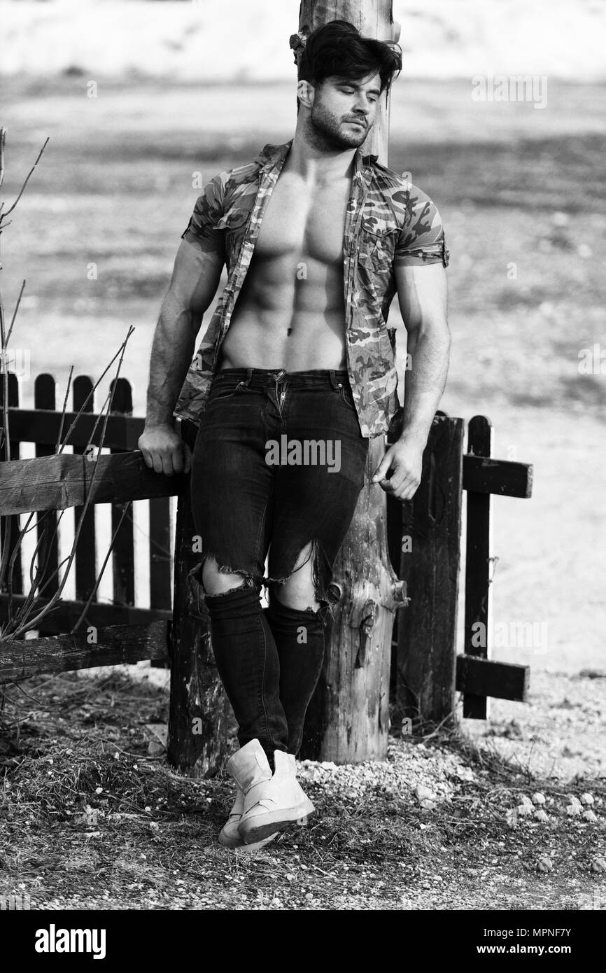 healthy young man standing strong flexing muscles while wearing black jeans muscular athletic bodybuilder fitness model posing outdoors a place fo MPNF7Y