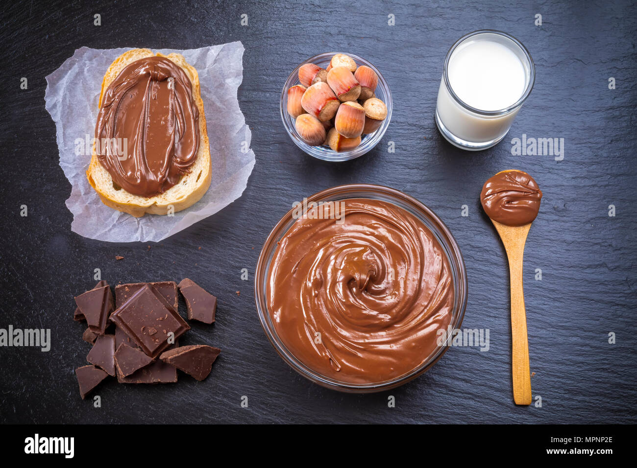 Slice of bread with spread chocolate cream and hazelnuts on black table