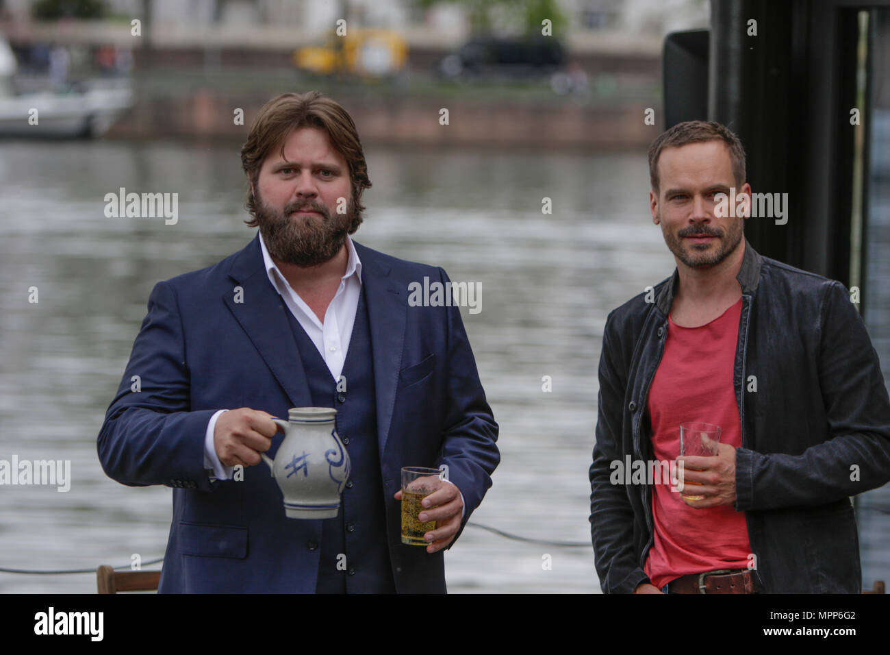 Frankfurt, Germany. 24th May 2018. Actors Antoine Monot, Jr. (left) and Wanja Mues (right) pose on the terrace of the houseboat that is owned by Mues' character Leo in the TV show with two glasses of cider and a Bembel (a local type of stoneware jug, used for cider). 4 new episodes of the relaunch of the long running TV series 'Ein Fall fuer zwei’ (A case for two) are being filmed in Frankfurt for the German state TV broadcaster ZDF (Zweites Deutsches Fernsehen). It stars Antoine Monot, Jr. as defence attorney Benjamin ‘Benni’ Hornberg and Wanja Mues as private investigator Leo Oswald. The epi Stock Photo