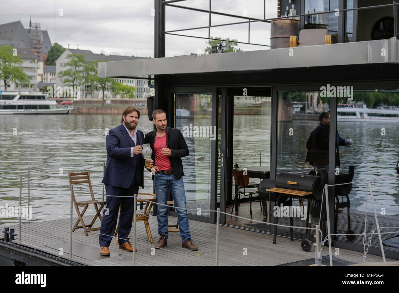 Frankfurt, Germany. 24th May 2018. Actors Antoine Monot, Jr. (left) and Wanja Mues (right) pose on the terrace of the houseboat that is owned by Mues' character Leo in the TV show with two glasses of cider and a Bembel (a local type of stoneware jug, used for cider). 4 new episodes of the relaunch of the long running TV series 'Ein Fall fuer zwei’ (A case for two) are being filmed in Frankfurt for the German state TV broadcaster ZDF (Zweites Deutsches Fernsehen). It stars Antoine Monot, Jr. as defence attorney Benjamin ‘Benni’ Hornberg and Wanja Mues as private investigator Leo Oswald. The epi Stock Photo