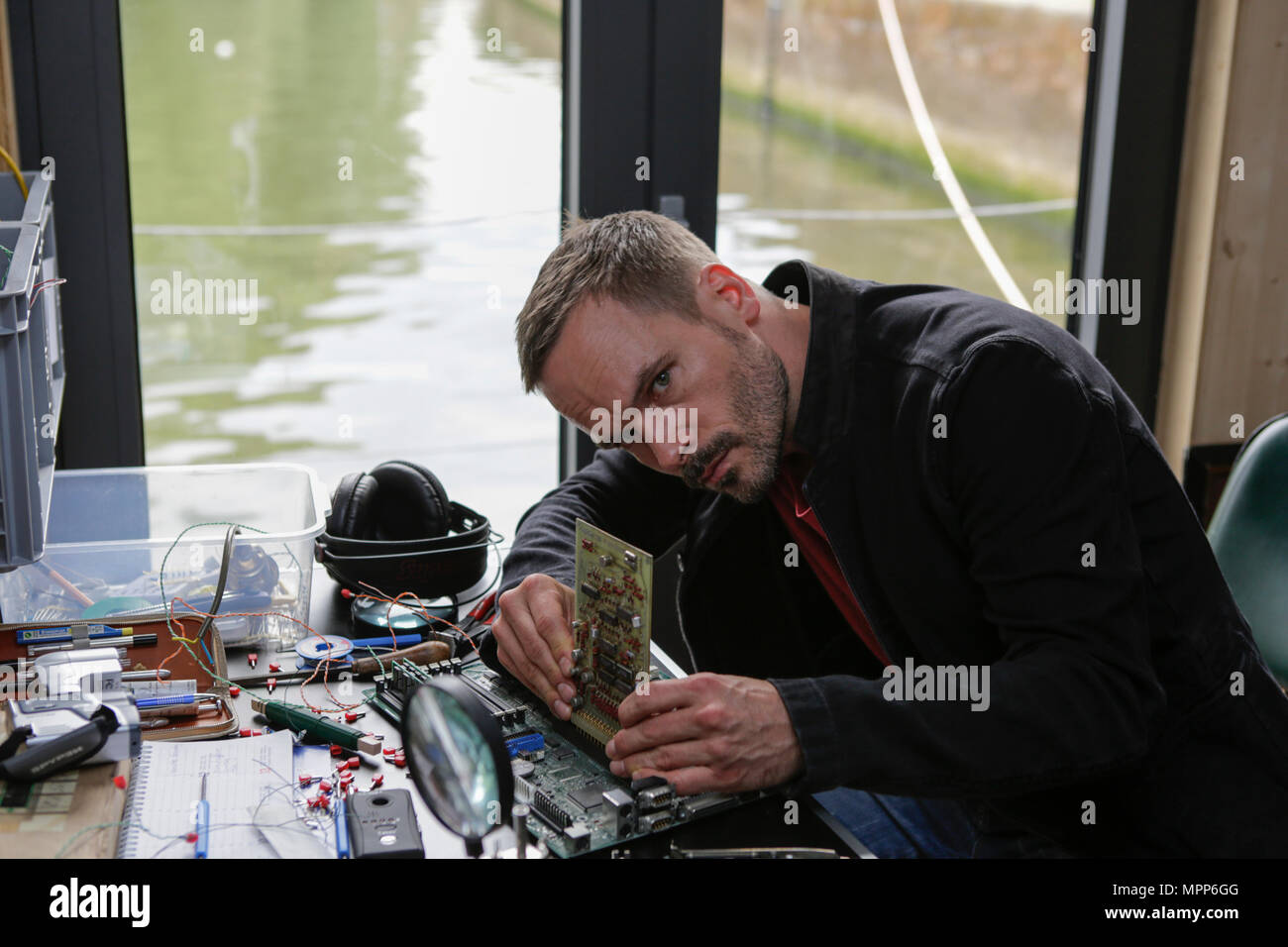 Frankfurt, Germany. 24th May 2018. Actors Wanja Mues poses on the desk in the houseboat that is owned by Mues' character Leo in the TV show, working on a computer circuit board. 4 new episodes of the relaunch of the long running TV series 'Ein Fall fuer zwei’ (A case for two) are being filmed in Frankfurt for the German state TV broadcaster ZDF (Zweites Deutsches Fernsehen). It stars Antoine Monot, Jr. as defence attorney Benjamin ‘Benni’ Hornberg and Wanja Mues as private investigator Leo Oswald. The episodes are directed by Thomas Nennstiel. The episodes are set to air in October. Stock Photo