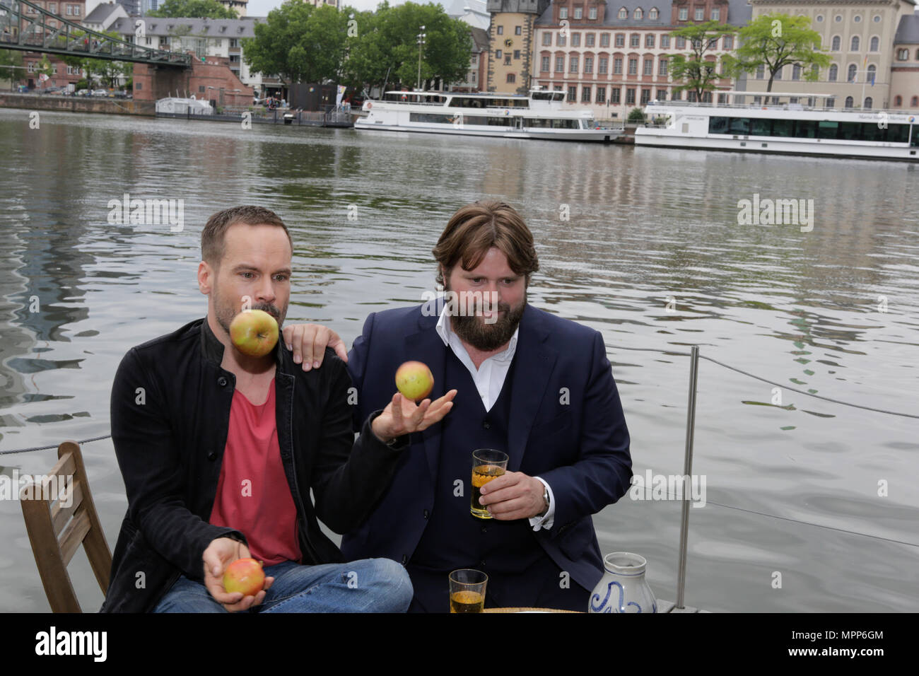 Frankfurt, Germany. 24th May 2018. Actors Wanja Mues (left) and Antoine Monot, Jr. (right) pose on the terrace of the houseboat that is owned by Mues' character Leo in the TV show with two glasses of cider and a Bembel (a local type of stoneware jug, used for cider).  Wanja Mues juggles three apples. 4 new episodes of the relaunch of the long running TV series 'Ein Fall fuer zwei’ (A case for two) are being filmed in Frankfurt for the German state TV broadcaster ZDF (Zweites Deutsches Fernsehen). It stars Antoine Monot, Jr. as defence attorney Benjamin ‘Benni’ Hornberg and Wanja Mues as privat Stock Photo