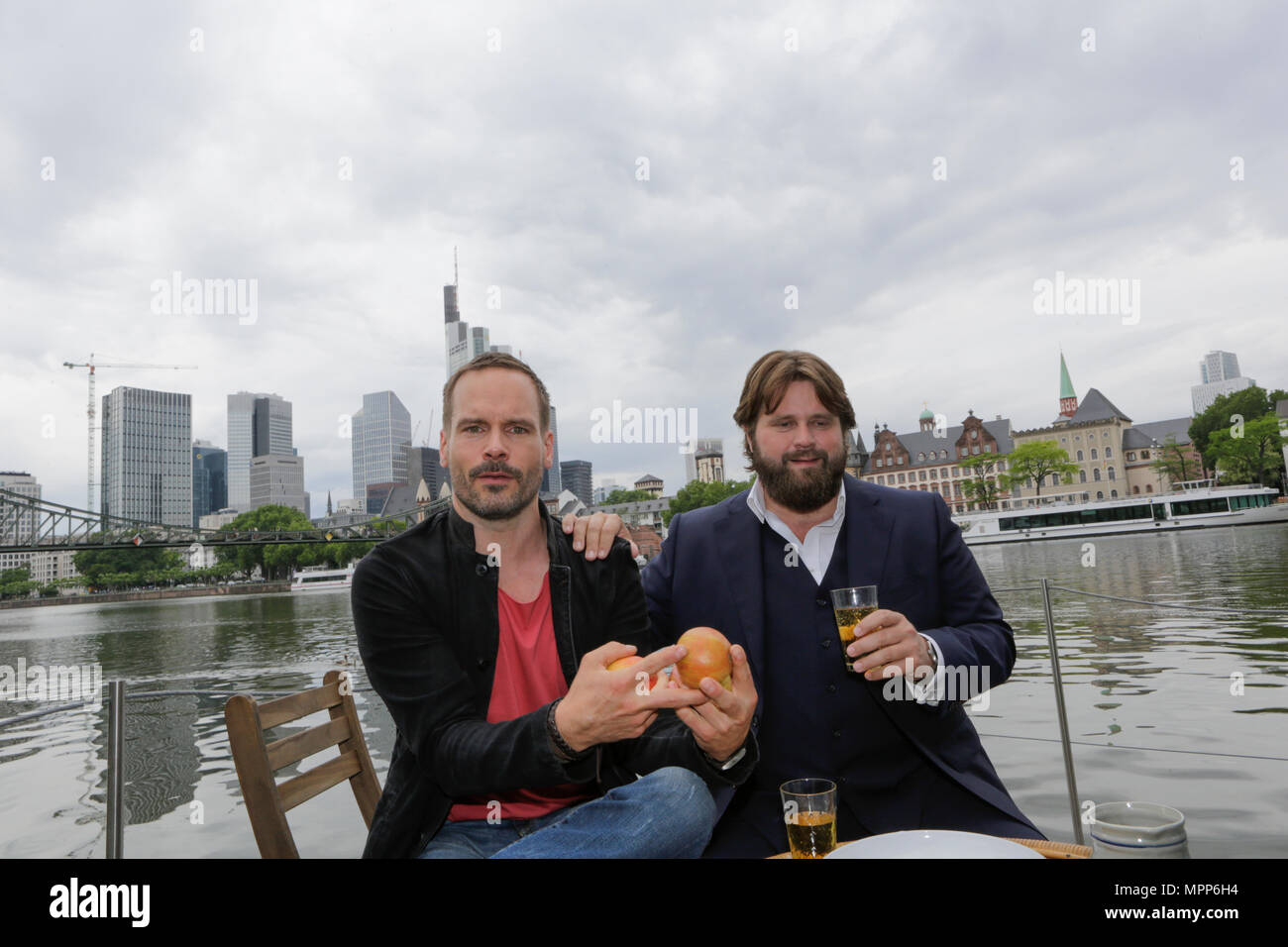 Frankfurt, Germany. 24th May 2018. Actors Wanja Mues (left) and Antoine Monot, Jr. (right) pose on the terrace of the houseboat that is owned by Mues' character Leo in the TV show with two glasses of cider and a Bembel (a local type of stoneware jug, used for cider).   4 new episodes of the relaunch of the long running TV series 'Ein Fall fuer zwei’ (A case for two) are being filmed in Frankfurt for the German state TV broadcaster ZDF (Zweites Deutsches Fernsehen). It stars Antoine Monot, Jr. as defence attorney Benjamin ‘Benni’ Hornberg and Wanja Mues as private investigator Leo Oswald. The e Stock Photo