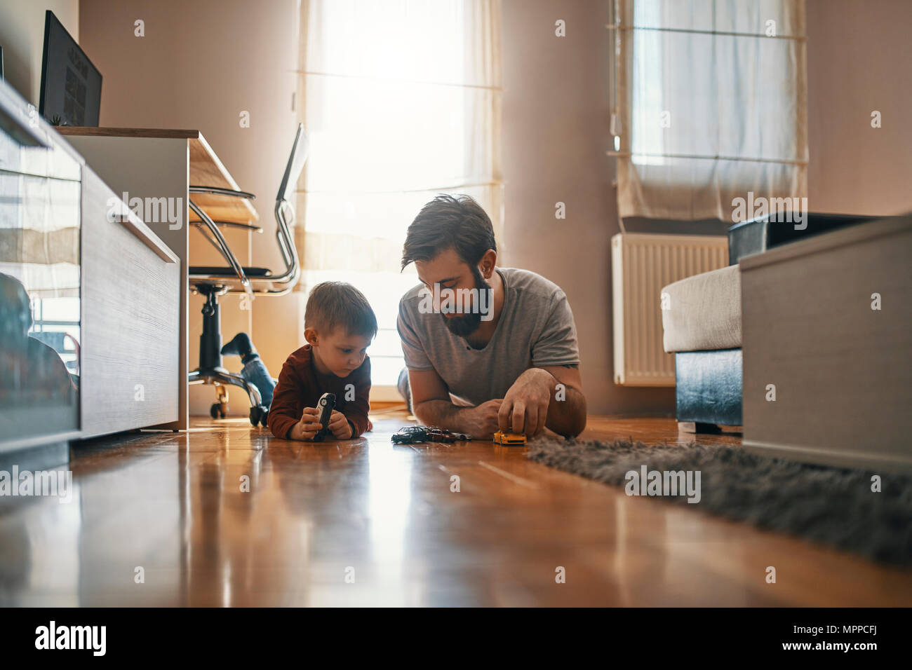 Father and son lying together on the floor playing with toy cars Stock Photo