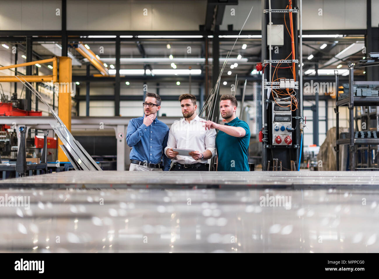 Three men sharing tablet on factory shop floor Stock Photo