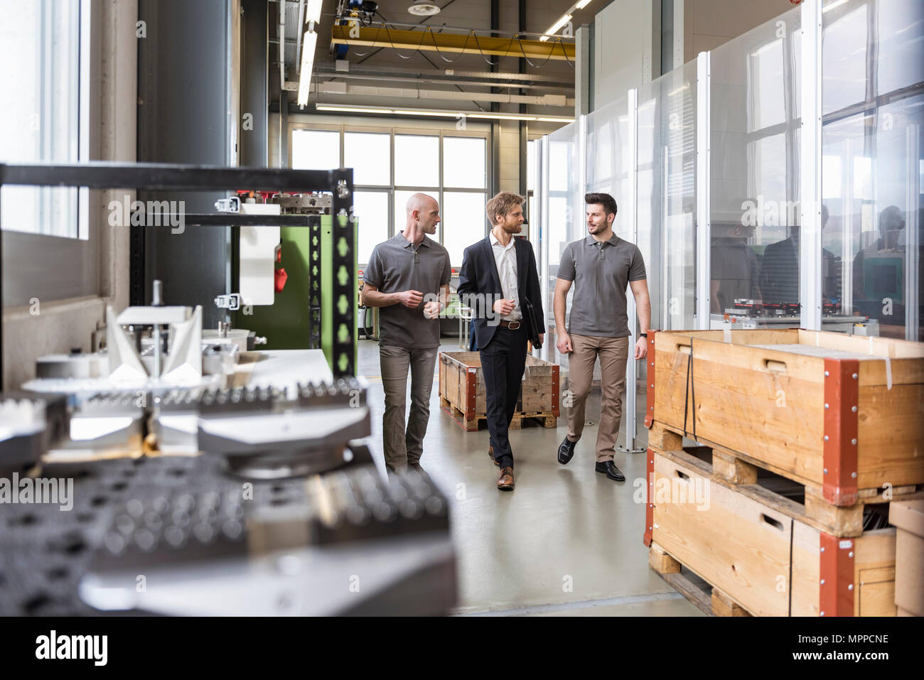 Three men walking and talking in factory Stock Photo