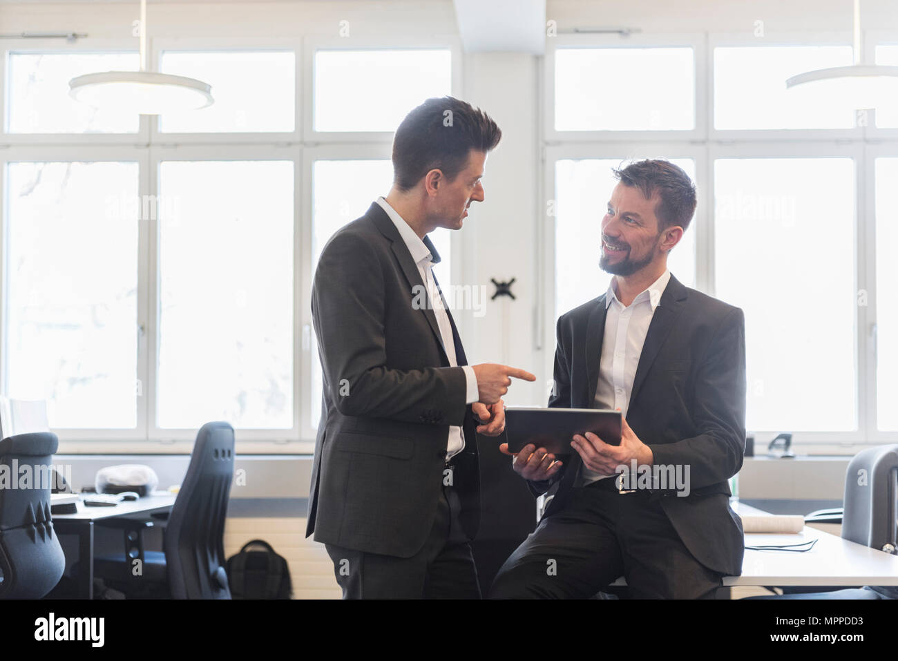Two businessmen standing in office, discussing solutions, using digital tablet Stock Photo