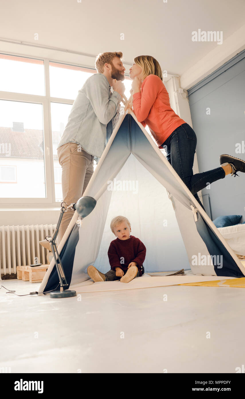 Happy couple kissing over tent with their son sitting in it Stock Photo