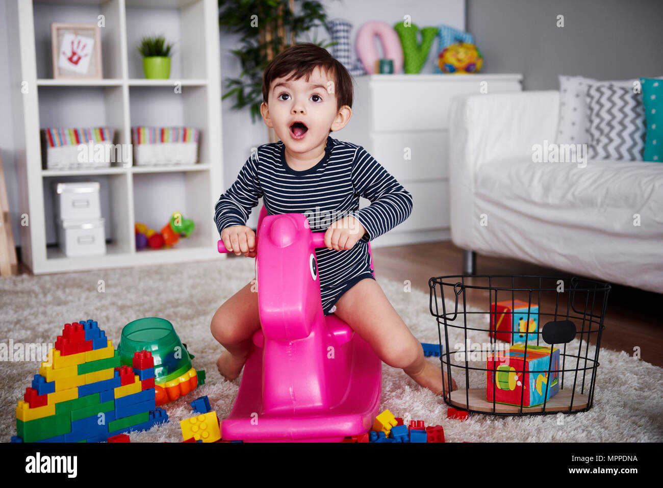 Portrait of little boy sitting on pink rocking horse in the living room Stock Photo