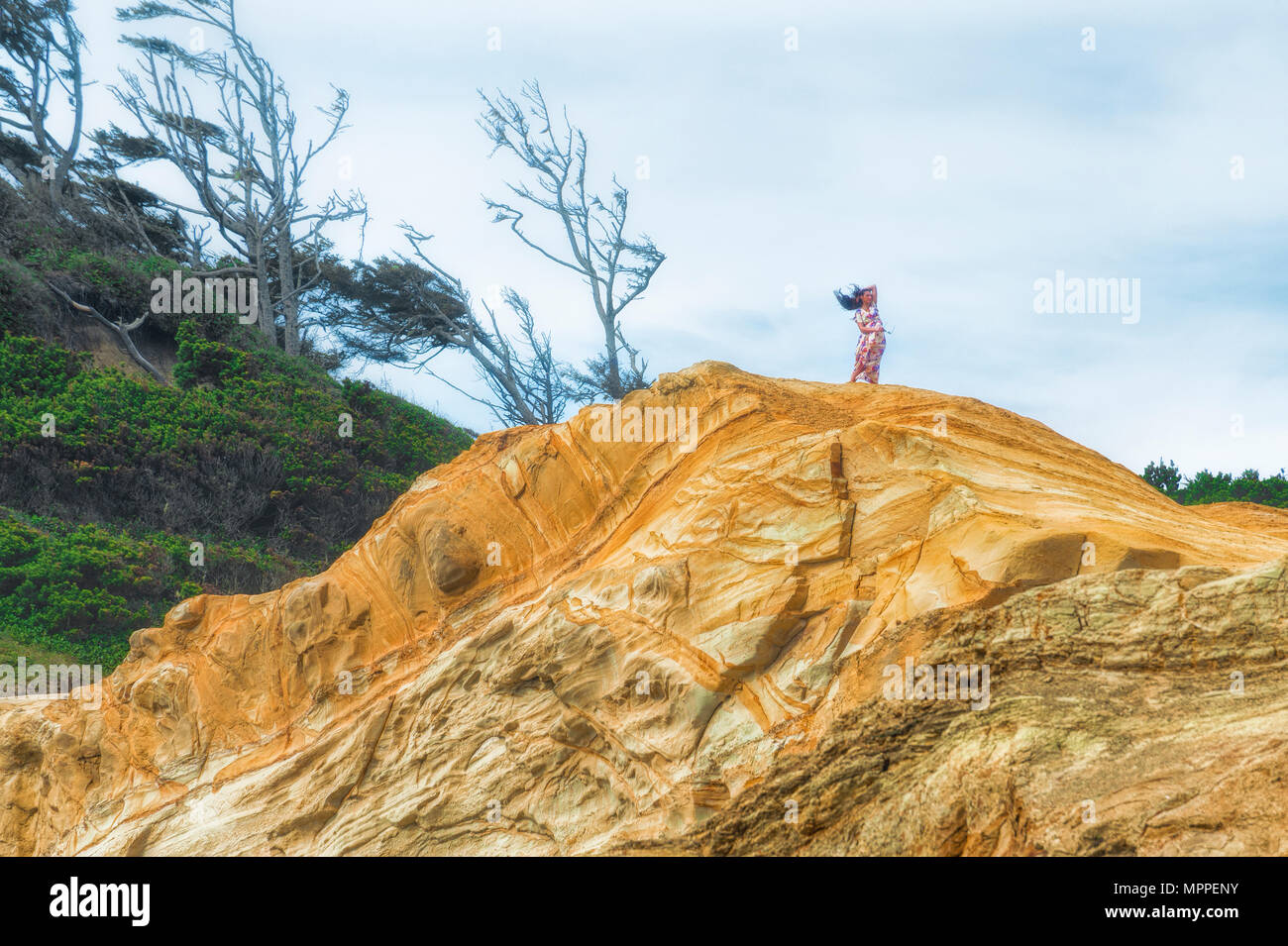 Pacific City, Oregon, USA - September 13, 2015:  A young woman in a long dress with long hair stands on top of a sandstone bluff.  Her long hair and d Stock Photo