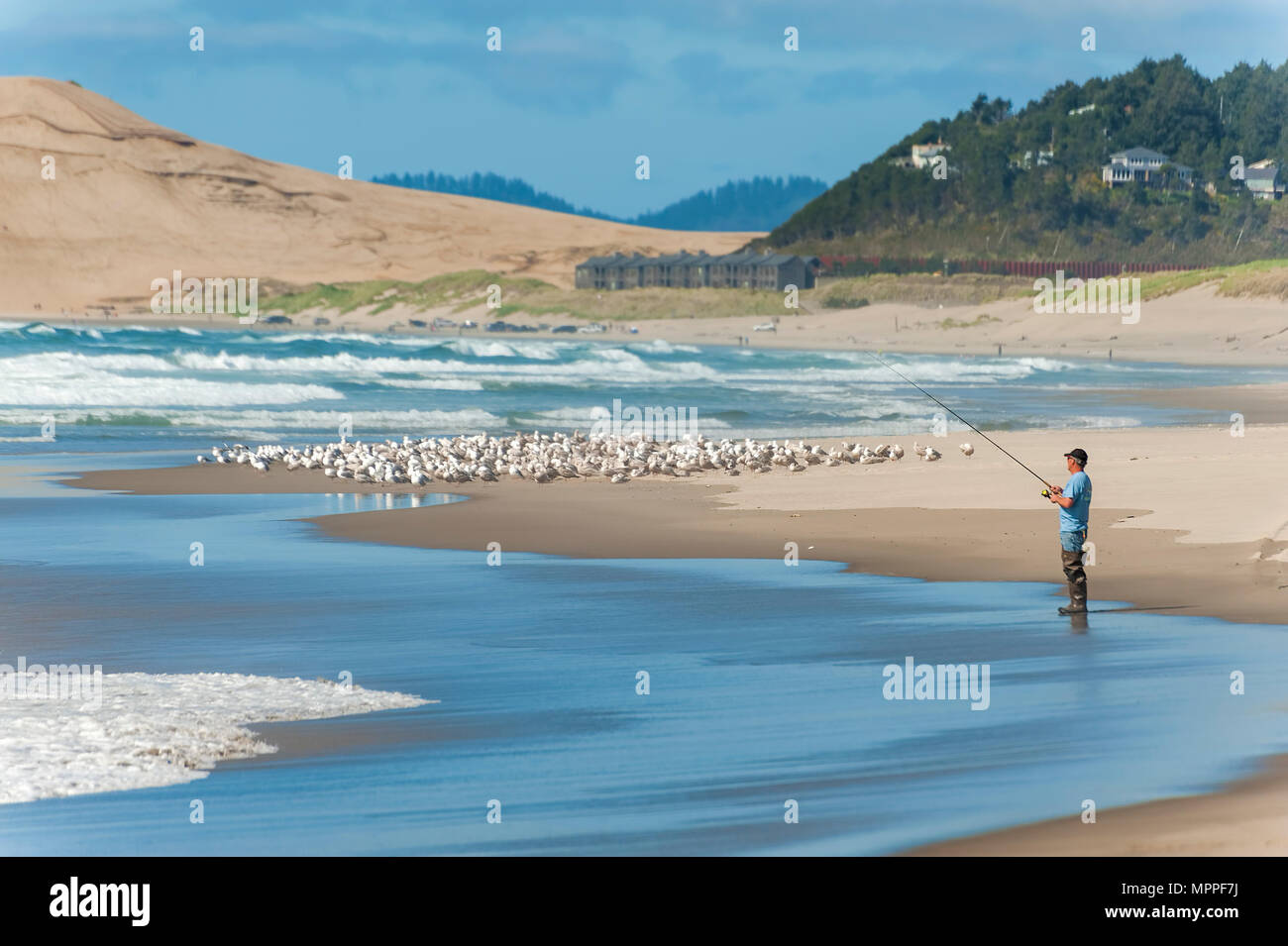 A view of the beach at Pacific City.  A fisherman can be seen wearing waders fishing in the surf. Stock Photo