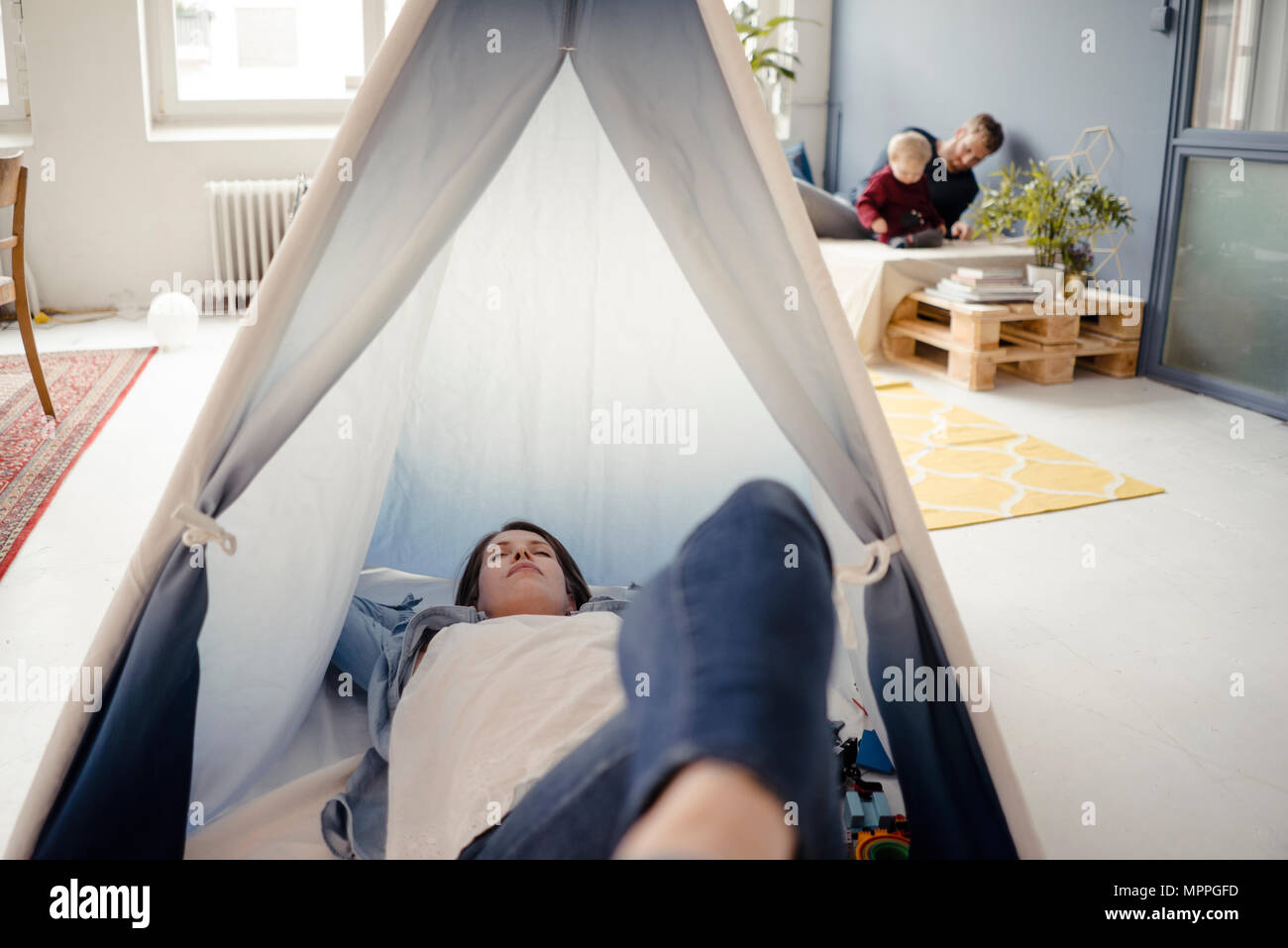 Woman resting in tent , while father is playing with their son in background Stock Photo