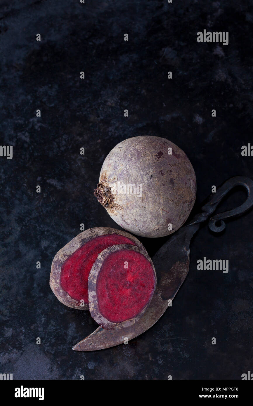 Whole and sliced beetroot and an old knife on dark metal Stock Photo