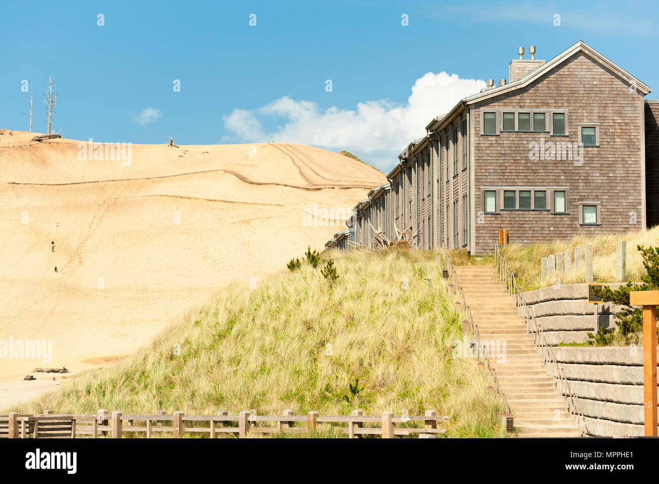 Pacific City lodging on a hill covered by grass with an even larger hill of sand in the background against a blue sky and white clouds Stock Photo