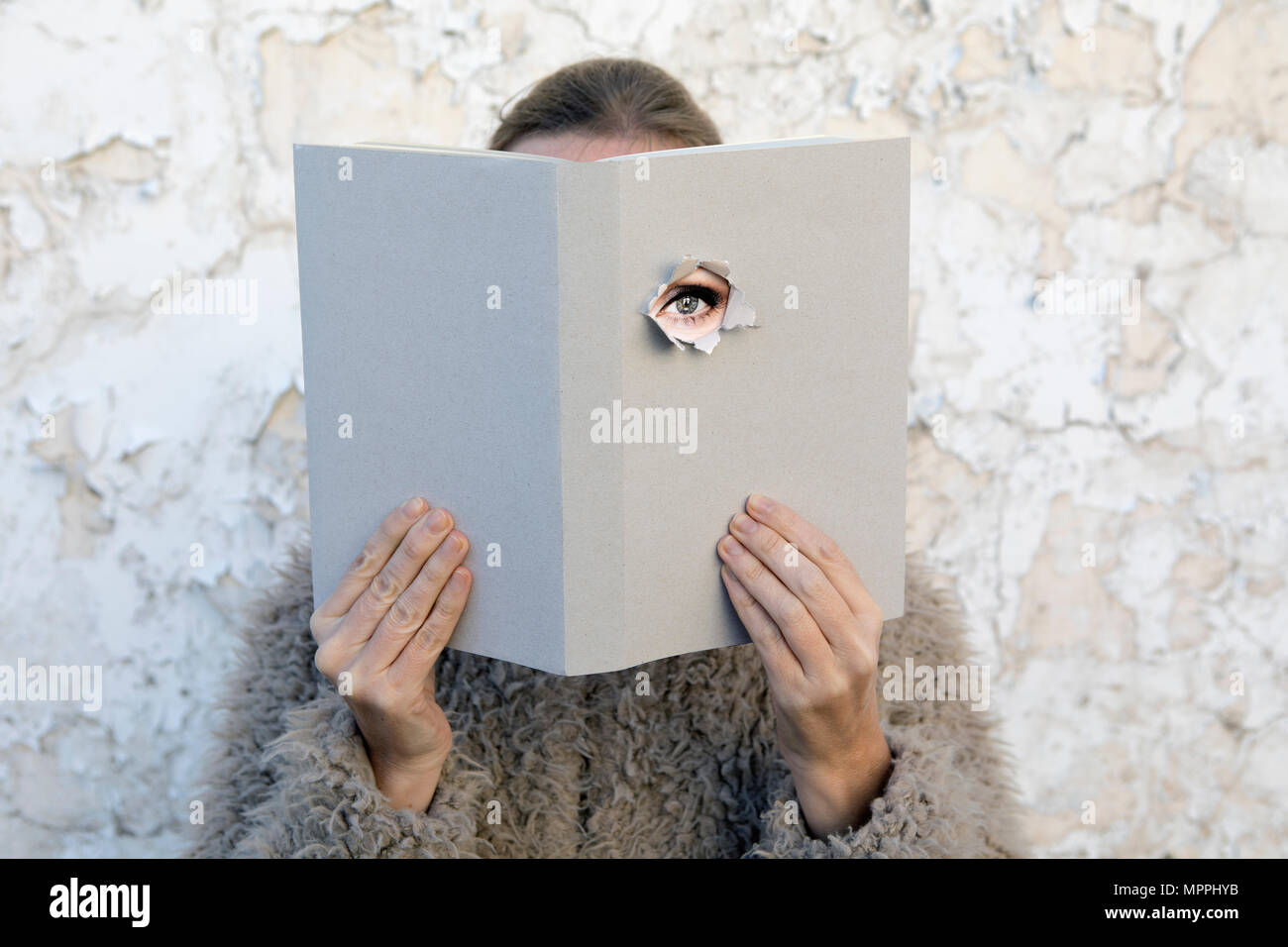 Woman covering face with book, reading poetry, eye looking through cover Stock Photo