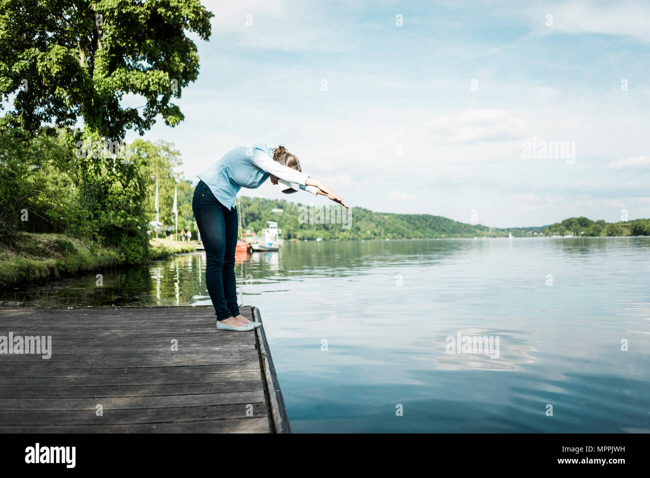 Woman on jetty wearing VR glasses pretending to dive into a lake Stock Photo