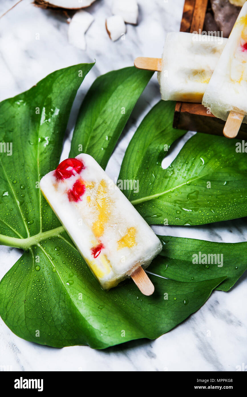 Pina Colada popsicle with candied cherries and pineapple on leaf Stock Photo