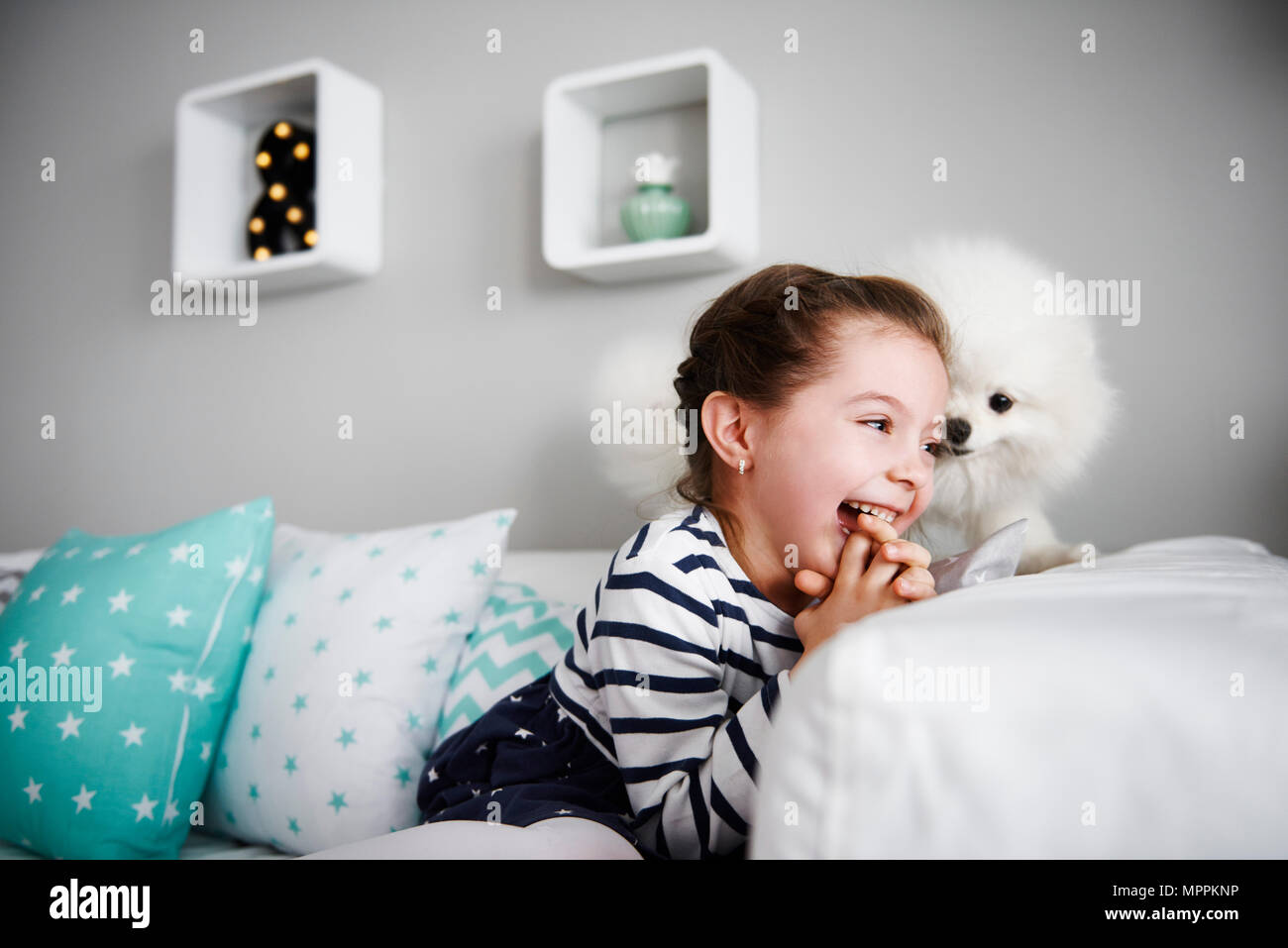 Laughing little girl playing with dog on the couch in the living room ...