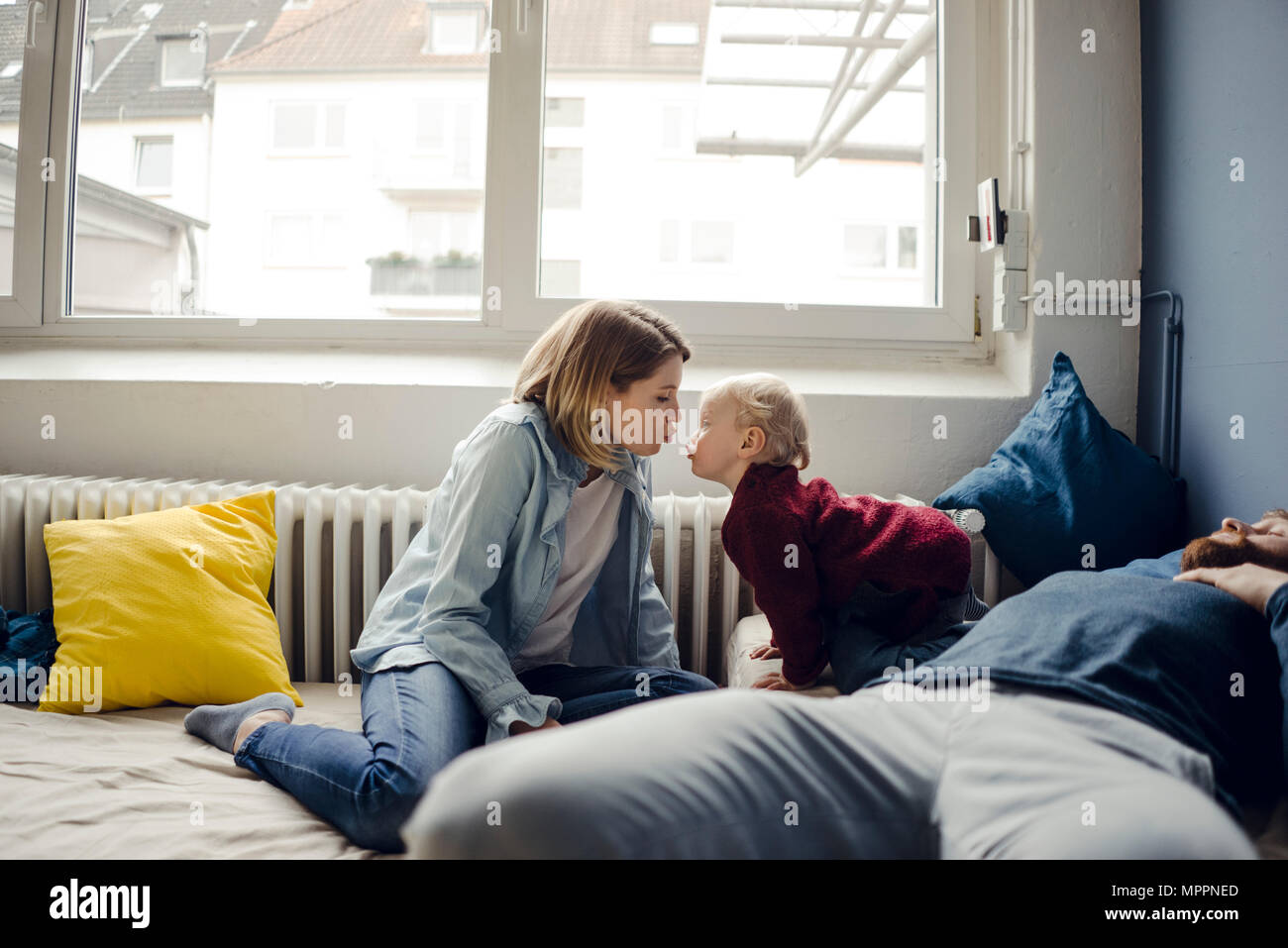 Family relaxing at home on the sofa, mother kissing baby son Stock Photo