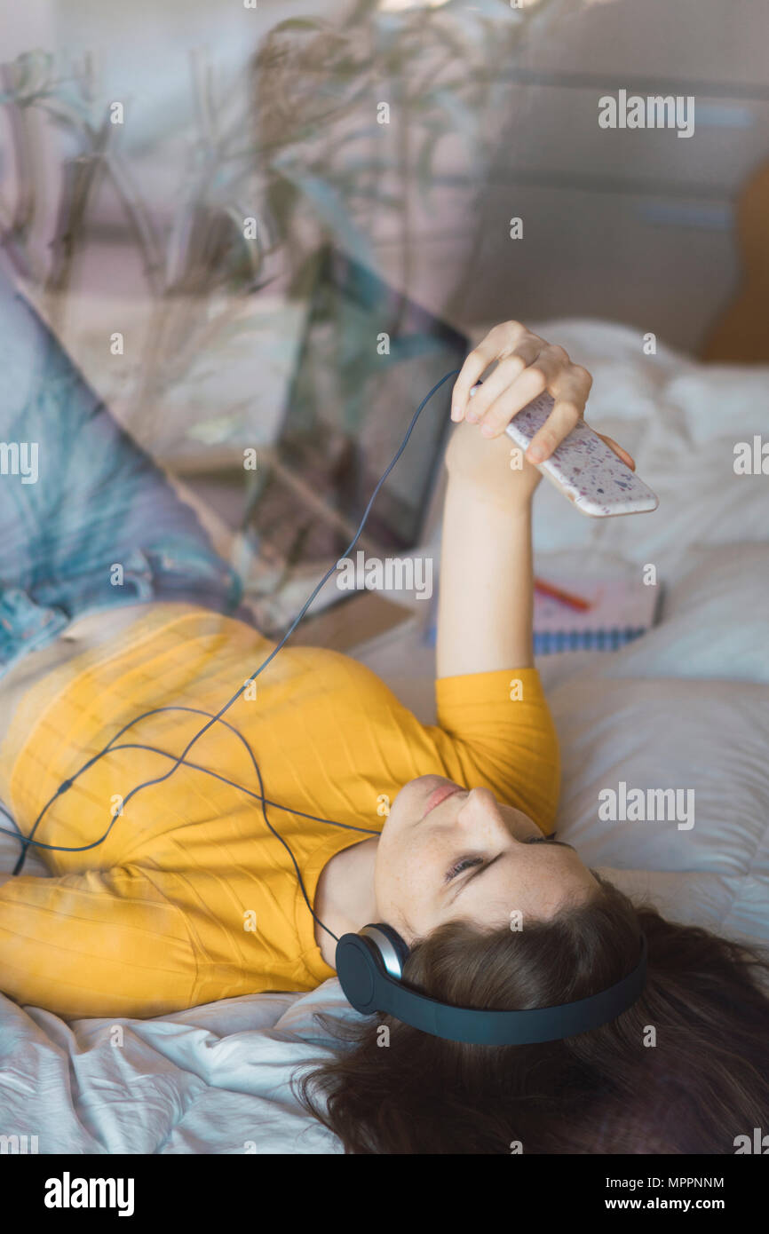 Young woman with headphones lying on bed taking selfie with smartphone Stock Photo