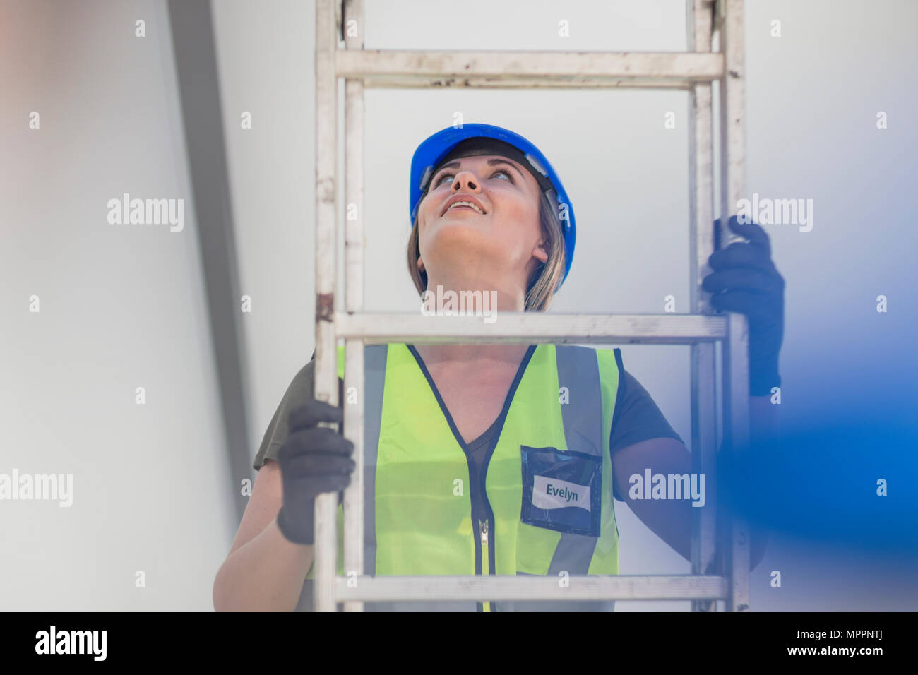 Young woman on construction site climbing ladder Stock Photo