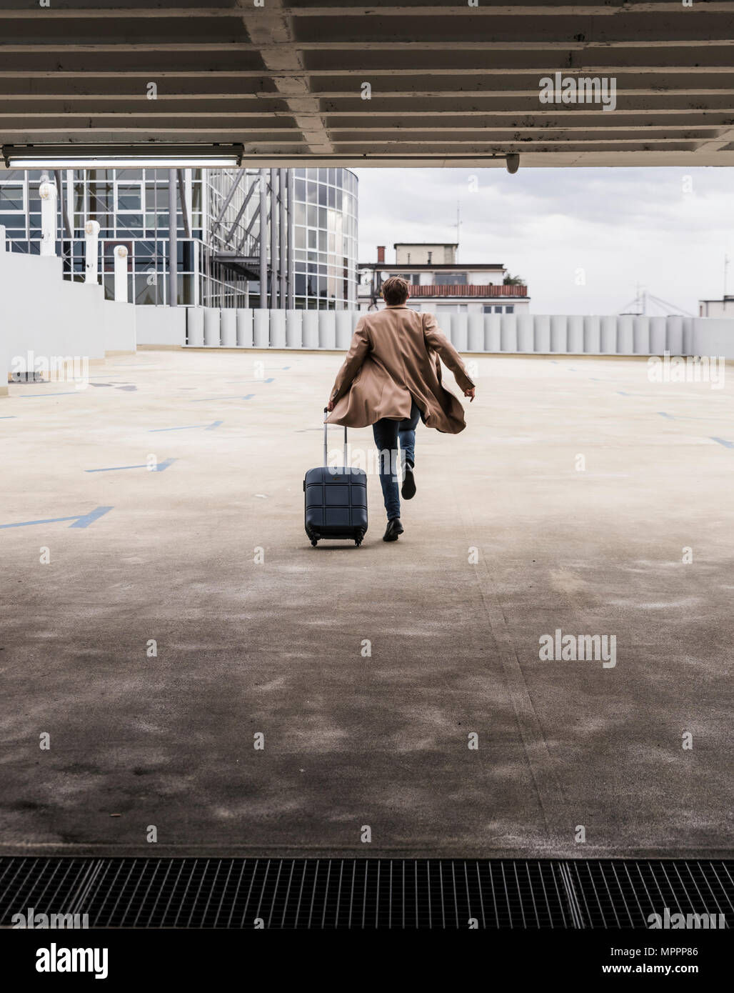 Businessman with rolling suitcase in a hurry at parking garage Stock Photo