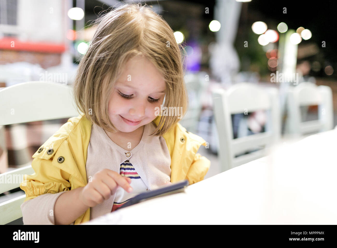 Portrait of smiling little girl sitting in a restaurant playing with smartphone Stock Photo