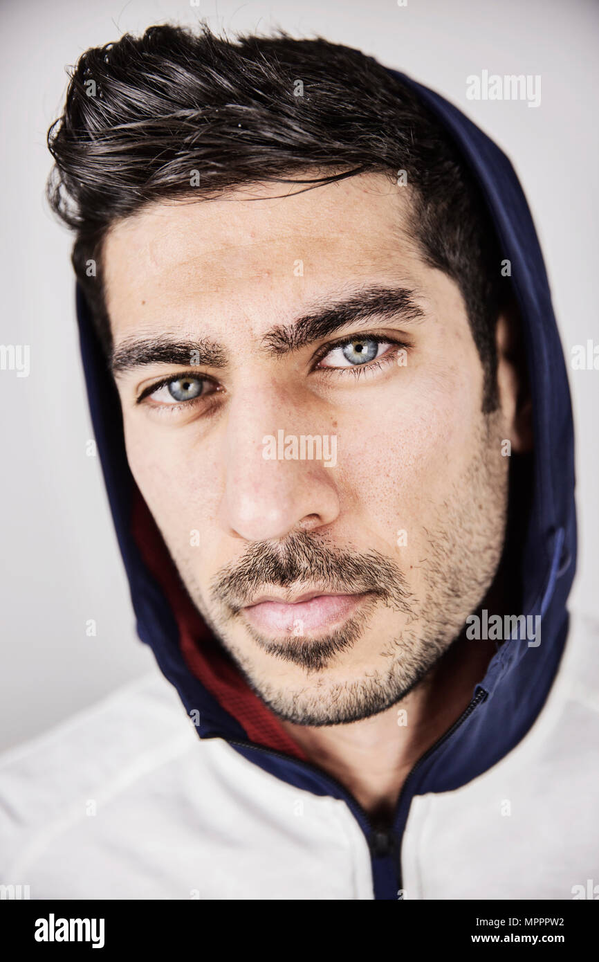 Portrait of serious young man with blue eyes and stubble wearing hoodes jacket Stock Photo