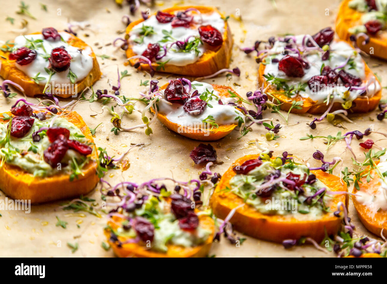 Slices of sweet potato with cream cheese, ramson cream, goat cheese, cress and cranberries Stock Photo