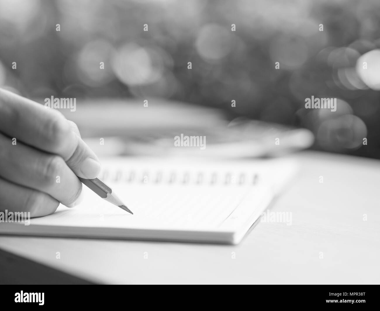 Closeup black and white  woman hand writing with red pencil, business document and note book on working table with nature green leaves background. Stock Photo