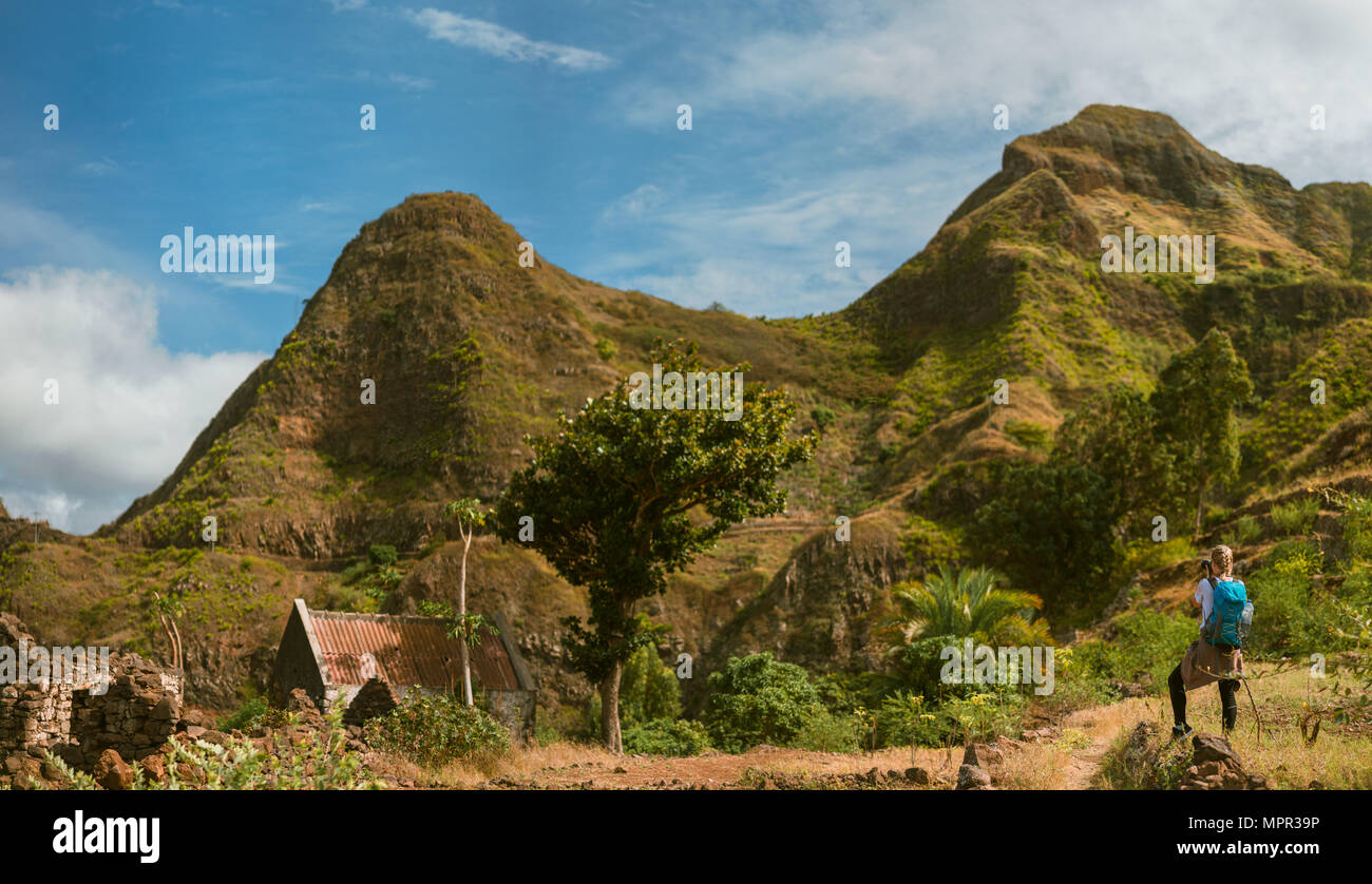 Panoramic view of woman tourist with blue backpack making photo of landscape in Mountains of Santo Antao island, Cabo Verde Stock Photo