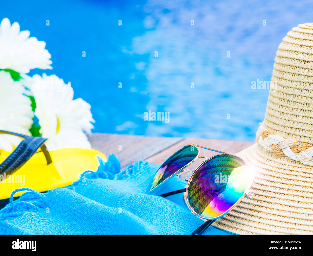Sunglasses with summer hat, flip flops and flowers by the swimming pool ...