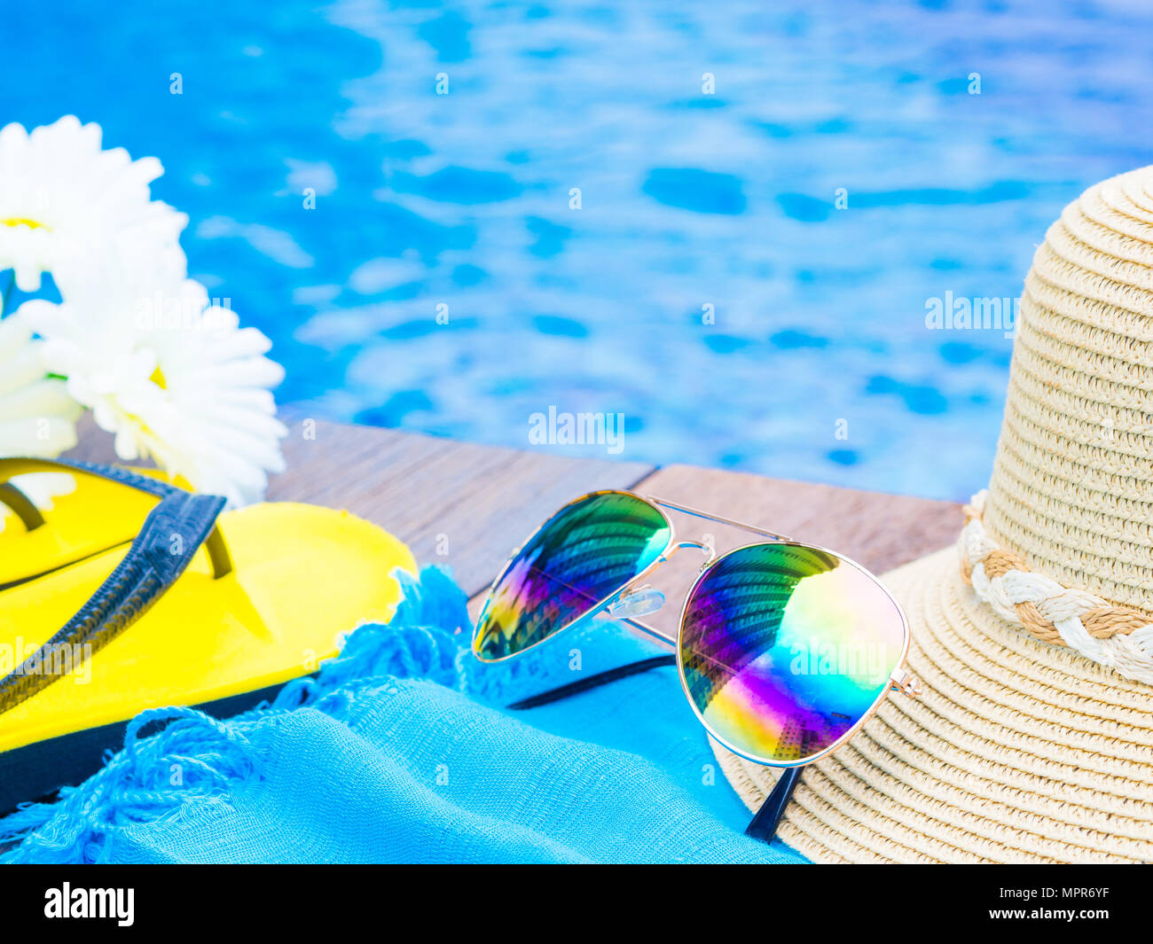 Sunglasses with summer hat, flip flops and flowers by the swimming pool ...