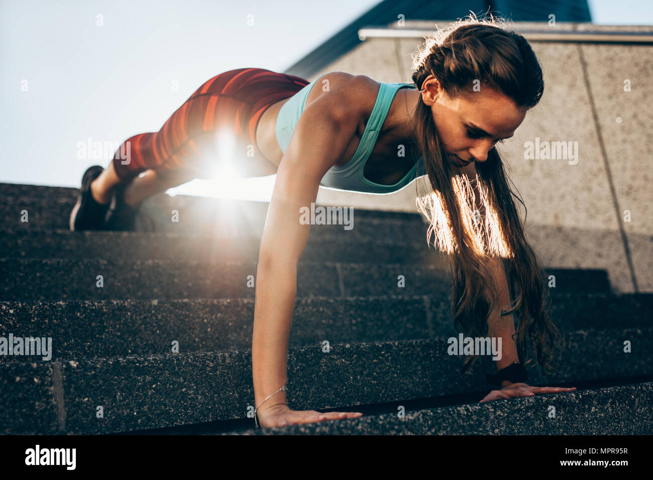 Strong young woman doing push ups on steps outdoors. Sportswoman doing push ups exercises in morning. Stock Photo