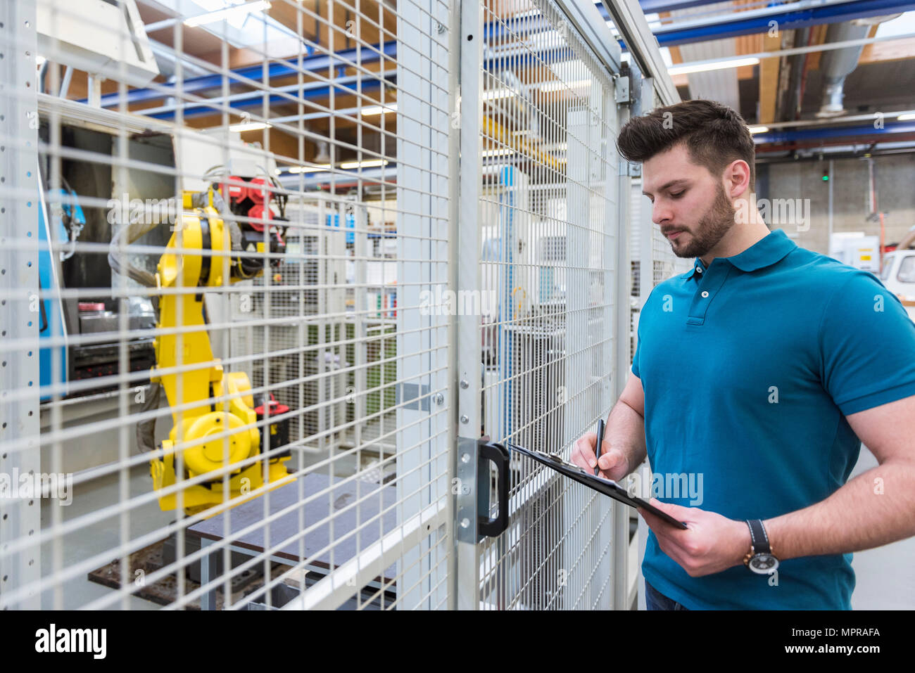 Man with clipboard standing at industrial robot in modern factory Stock Photo