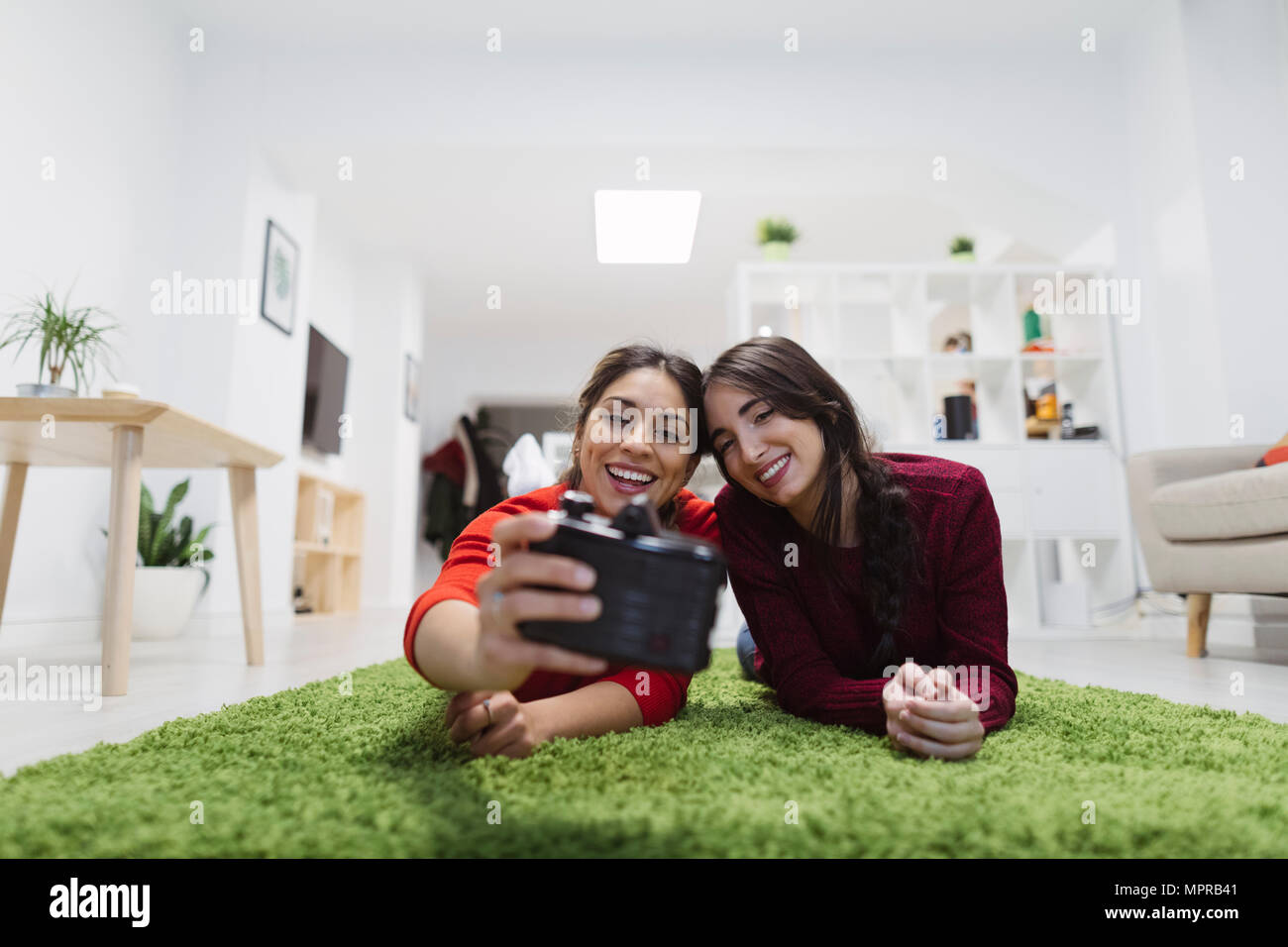 Two happy young women lying on the floor in coworking space taking a selfie Stock Photo