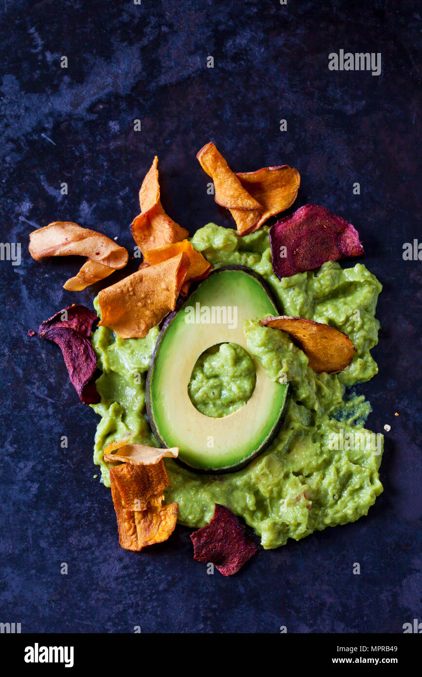 Guacamole, slice of avocado and vegetable chips on dark ground Stock Photo